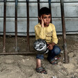 A boy in a yellow shirt kneels on the ground with an empty pot in his hands