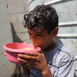 A boy wearing a striped t-shirt lifts a pink bowl to his lips