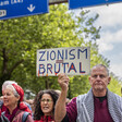 A man holds a placard saying Zionism Equals Brutal surrounded by other protesters