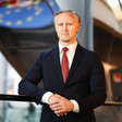 A man wearing a suit and tie stands in front of the blue and yellow logo of the European Union