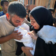 A crying man and woman look at a shrouded baby held by the woman