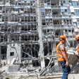 Two workers stand in front of badly damage facade of tall building