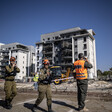 Personnel in uniform stand in front of damaged apartment buildings