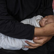 A woman's arms, clothed in black, cradles a sleeping newborn baby wrapped in a white blanket.