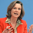 A portrait of a woman wearing a red jacket speaking at an event 