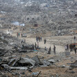 People walk on a road amid a landscape of destruction.