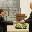 Israel's President Issac Herzog holds a leather-bound folder on one side as the European Union diplomat Michael Mann holds it on the other side.