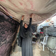 A woman in dark clothing holds her hands up, touching a swath of fabric over her shelter