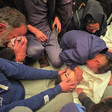 Mourners kneel on the floor, grieving over the body of a youth wrapped in a white shroud