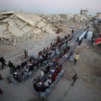 Palestinians sit along a long table for an Iftar feast. There are demolished buildings around them.