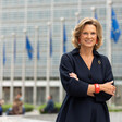 The European Union's Coordinator Against Anti-Semitism Katharina von Schnurbein stands with her arms folded outside a building with poles to which blue and yellow flags are attached 