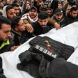 Group of men carries a shrouded body with a bulletproof press vest and flowers on top of it