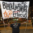 A protester holds a banner reading Black Lives Matter Trump Can't Erase Us