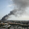 A wide urban landscape with thick smoke rising from a large building