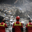 Three first responders stand in front of badly damaged building.