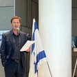 Man holds a piece of paper as he stands behind a microphone stand with flags of Israel and Germany beside him 