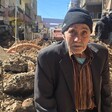 Older man sits in front of rubble of a bombed building