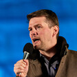 Man speaks into a microphone with a blue backdrop behind him 