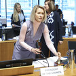 The European Union's Kaja Kallas stands and holds a small bell on a desk bearing papers and refreshments 