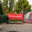 A man stands beside a red sign with the logo of the firm Leonardo and graffiti reading Palestina Libera on it  