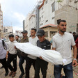 A group of men carry a small body wrapped in a white shroud.