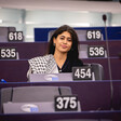 Elected representative Rima Hassan wears a checkered scarf or kuffiyeh as she sits at a desk numbered 454 and bearing the European Parliament logo