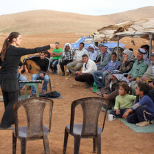 Women in black gesture towards audience in outdoor setting