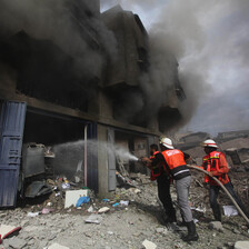 Firefighters aim hose at building billowing with smoke