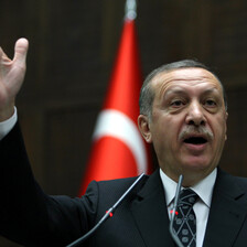 Turkish prime minister seen gesturing with hand in front of flag of Turkey