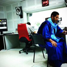 Man wearing blue robe looks at his phone in a radio station suite