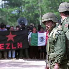 Mexican soldiers stand in front of crowd of protesters holding flags