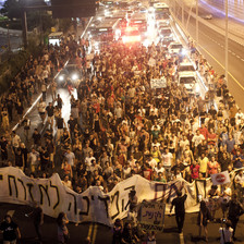 Protesters march down a highway carrying banners and signs