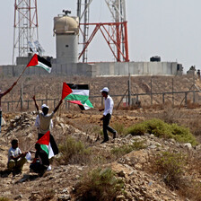 Youths holding Palestinian flags stand in front of Israel's border wall and military jeep