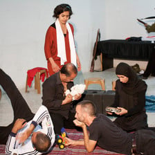 Scene from play shows family sitting together in foreground with Israeli soldier character in background