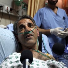 Man on hospital bed surrounded by microphones