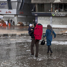 Couple carrying baby cross flooded street in war-torn camp