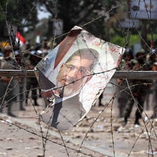 A poster of Mohammed Morsi entangled in barbed wire, with soldiers in background