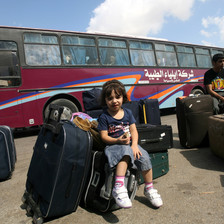 Girl sits amid suitcases in front of bus