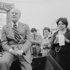 Woman writes on notepad as man sits on desk