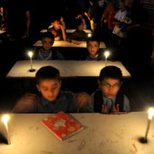 Boys sit at school desks in room lit with candles