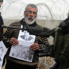 Middle-aged man holds photo of Mandela in front of heavily armed Israeli soldier