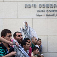 Men wearing checkered scarves hold banners outside court house