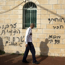 Man walks in front of stone wall spray painted with Hebrew graffiti