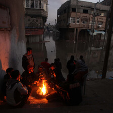 Men sit by campfire in flooded urban area