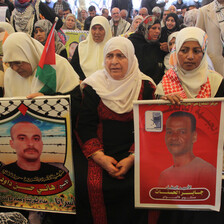 Elderly woman sits amongst crowd holding posters of Palestinian prisoners