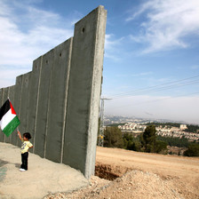 Girl holding Palestine flag stands next to section of 25-foot-tall concrete wall under construction