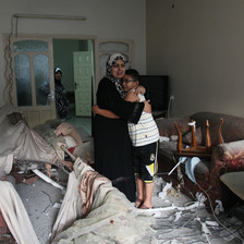 A mother hugs her adolescent son in a bombed-out living room