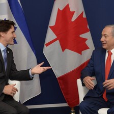 Two men sitting in chairs in front of flags