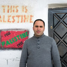 Young man stands in front of wall reading This is Palestine