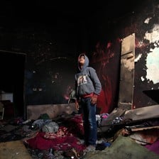 A boy stands in the middle of a room with charred walls and debris